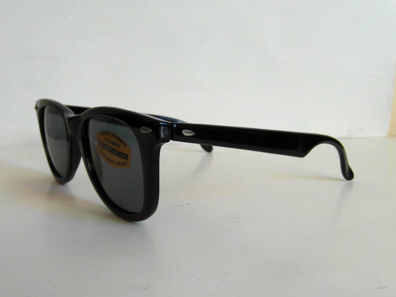 May include: Black plastic sunglasses with dark lenses. The sunglasses have a label on the right lens that says "Vesper Temples, Ultraviolet Absorbents, Polarized Lenses".