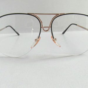 Könnte beinhalten: Transparente Aviator-Brille mit schwarzem Rahmen und goldener Metallbrücke.