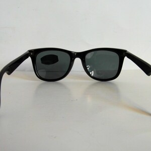 May include: Black plastic sunglasses with dark gray lenses. The sunglasses have a classic square shape and are shown from the back.