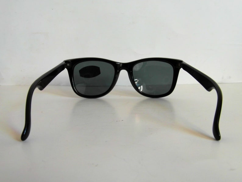 May include: Black plastic sunglasses with dark gray lenses. The sunglasses have a classic square shape and are shown from the back.
