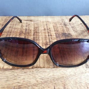 Puede incluir: Un par de gafas de sol de carey marrón y negro con lentes marrones. Las gafas tienen un borde decorativo con tachuelas alrededor de las lentes.