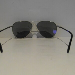 K&ouml;nnte beinhalten: Silberne Aviator-Sonnenbrille mit dunkelgrauen Gl&auml;sern. Die Sonnenbrille hat einen schwarzen Rahmen und wird von hinten gezeigt.