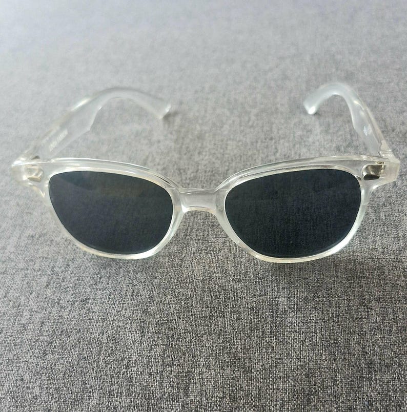 Peut inclure: Lunettes de soleil &agrave; monture transparente avec verres fonc&eacute;s. Les lunettes ont un design classique et r&eacute;tro avec une monture et des branches l&eacute;g&egrave;rement incurv&eacute;es. Les verres sont noirs, contrastant avec la monture transparente. Un accessoire &eacute;l&eacute;gant.