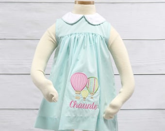 May include: A light blue sleeveless dress with a white Peter Pan collar and a gingham pattern. The dress features an embroidered design of three hot air balloons and the name "Chaunte" in pink thread.