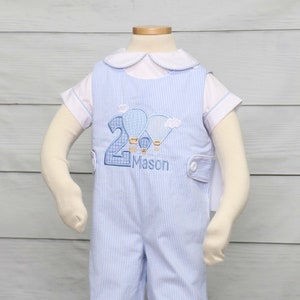 May include: Blue and white striped romper with a white collared shirt underneath. The romper features an embroidered design of hot air balloons, the number 2, and the name "Mason". The outfit is designed for a child's second birthday.