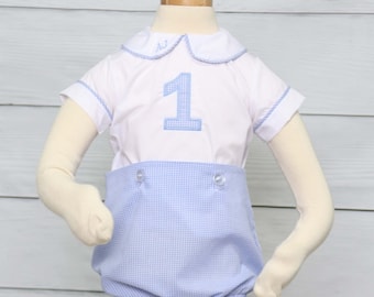 Puede incluir: Un conjunto blanco y azul para un niño de un año. La parte superior tiene el número 1 bordado en azul y las iniciales "AJ" en el cuello. El conjunto incluye una camisa blanca con ribetes azules y un pantalón corto de cuadros azules. El conjunto se muestra en un maniquí.
