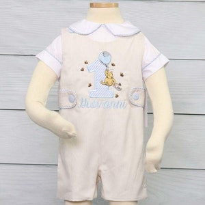 Boys first Birthday Outfit is a light khaki boys romper with side tabs and decorative buttons.  Shown with number 1 and classic winnie the pooh and available with or without monogram.  Matching shirt is also available.