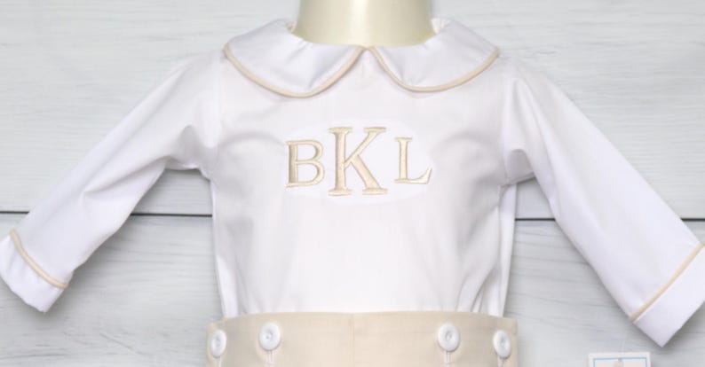 May include: White long-sleeve shirt with a beige collar and cuffs. The shirt has a beige embroidered monogram "BKL" on the front.