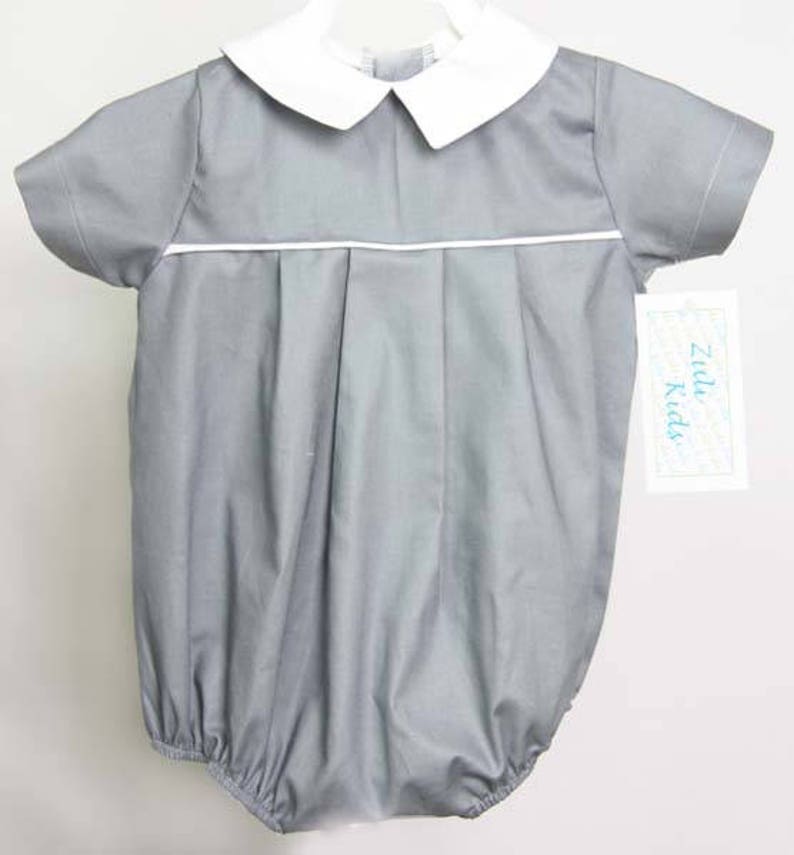 K&ouml;nnte beinhalten: Ein grauer Baby-Strampler mit wei&szlig;em Kragen und wei&szlig;em Besatz. Der Strampler hat Falten vorne und ein Zildy Kids-Etikett.