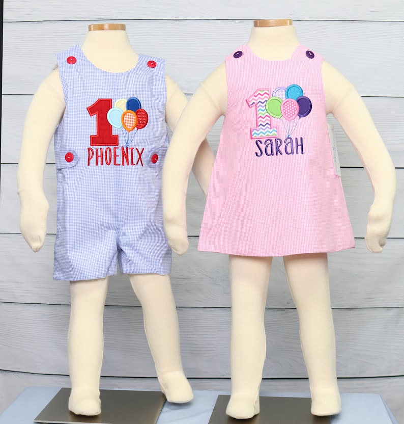 May include: Two baby outfits for a first birthday. A blue and white gingham romper with the number one and the name "Phoenix" embroidered on it. A pink gingham dress with the number one and the name "Sarah" embroidered on it. Both outfits feature colorful balloons.