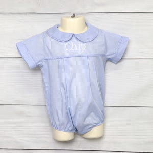 Puede incluir: Un pelele de bebé de gingham azul y blanco con un cuello blanco Peter Pan y el nombre "Chip" bordado en la parte delantera.
