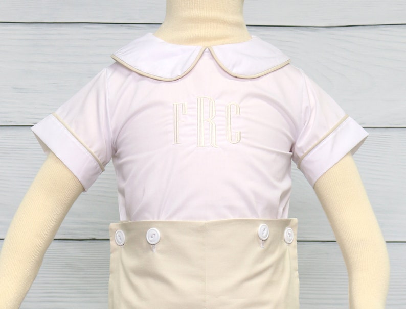 May include: A white short-sleeved button-down shirt with a tan collar and cuffs. The shirt has a tan trim around the collar and cuffs. The shirt is embroidered with the letters "TRC" in tan thread. The shirt is paired with tan shorts.