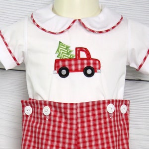 Puede incluir: Conjunto de beb&eacute; blanco con un dise&ntilde;o de cami&oacute;n de &aacute;rbol de Navidad rojo y verde. El conjunto presenta una camisa blanca con cuello y ribete rojo y pantalones cortos a cuadros rojos y blancos con botones blancos. Un atuendo festivo.