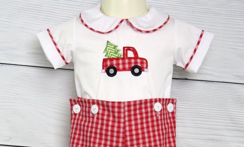 Puede incluir: Conjunto de beb&eacute; blanco con un dise&ntilde;o de cami&oacute;n de &aacute;rbol de Navidad rojo y verde. El conjunto presenta una camisa blanca con cuello y ribete rojo y pantalones cortos a cuadros rojos y blancos con botones blancos. Un atuendo festivo.