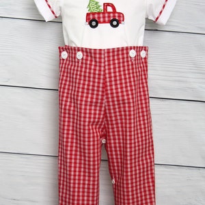 Puede incluir: Un conjunto navide&ntilde;o blanco y rojo para beb&eacute;. La parte superior tiene un cami&oacute;n rojo con un dise&ntilde;o de &aacute;rbol de Navidad. Los pantalones son de cuadros rojos y blancos con botones blancos. La parte superior tiene un cuello blanco con ribete rojo.