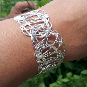 May include: A silver bracelet with a delicate, intricate design of overlapping circles and lines. The bracelet is open and adjustable.