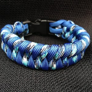 May include: A blue, white, and black paracord bracelet with a black plastic buckle closure.