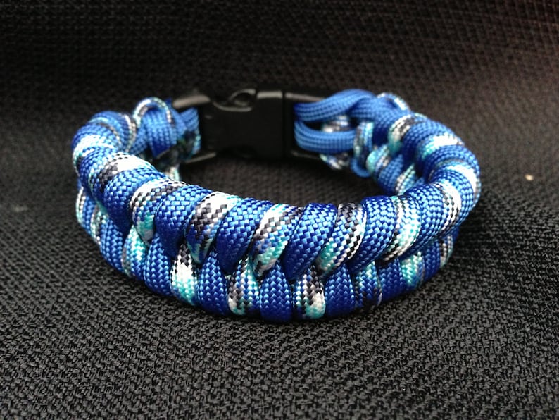 May include: A blue, white, and black paracord bracelet with a black plastic buckle closure.