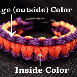 May include: A two-tone paracord bracelet with an orange edge (outside) color and a purple inside color. The bracelet is made with a woven pattern and has a black plastic clasp.