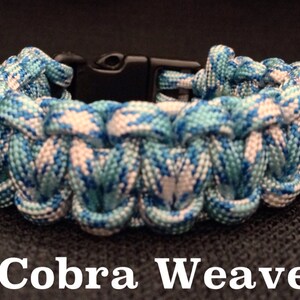 May include: A blue and white paracord bracelet with a black plastic clasp. The bracelet is woven in a cobra weave pattern. The text "Cobra Weave" is printed below the bracelet.