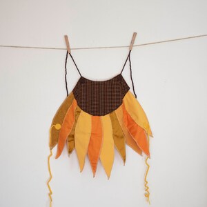 Peut inclure: Un costume de tournesol brun et jaune avec un centre &agrave; carreaux brun et blanc. Le costume est suspendu &agrave; une corde &agrave; linge avec des pinces &agrave; linge.