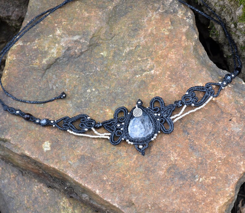 May include: A black macrame necklace with a silver and black beaded trim and a large, teardrop-shaped blue gemstone pendant.