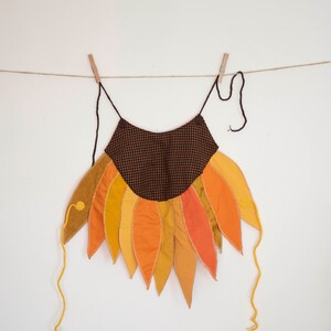Peut inclure: Un costume de tournesol en tissu &agrave; carreaux brun et noir avec des p&eacute;tales jaunes, orange et rouges. Le costume a une longue ficelle pour l'accrocher.