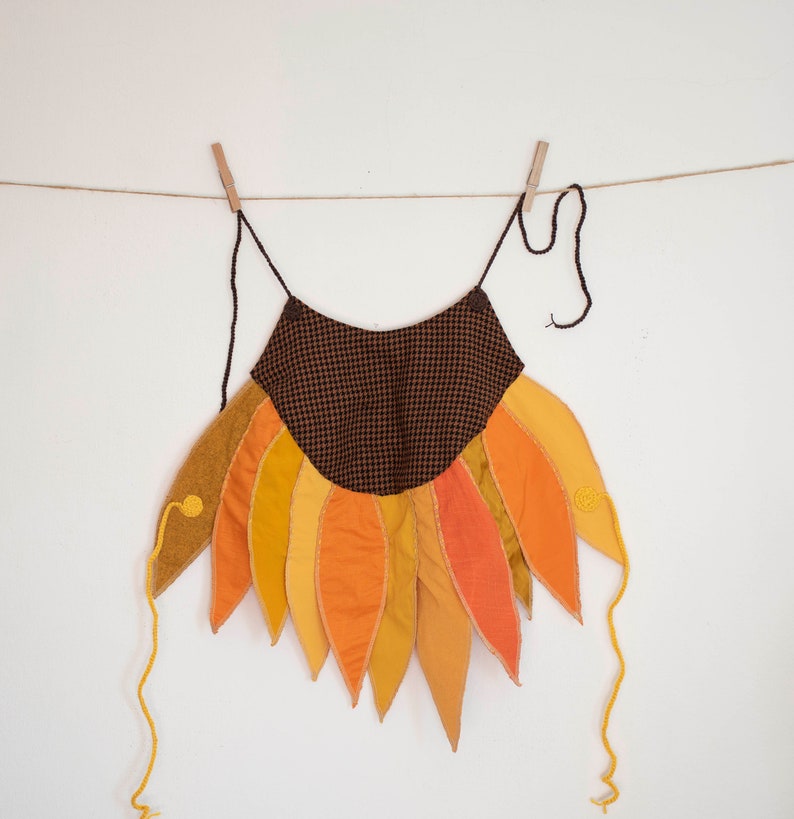 Peut inclure: Un costume de tournesol en tissu &agrave; carreaux brun et noir avec des p&eacute;tales jaunes, orange et rouges. Le costume a une longue ficelle pour l'accrocher.
