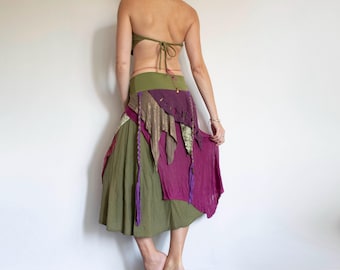 Peut inclure: Un haut dos nu vert olive avec des liens au dos et une jupe superposée composée de panneaux de tissu vert olive, violet foncé et doré métallisé. La jupe présente un ourlet asymétrique avec des franges tressées violettes.