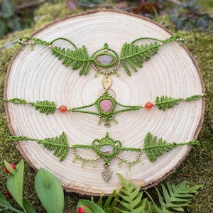 Puede incluir: Tres pulseras de macramé verde con diseños en forma de helecho y detalles de piedras preciosas. Las pulseras se muestran sobre una superficie de madera.