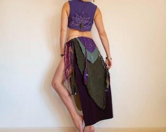 May include: A purple crop top with a lotus flower design and a layered skirt. The skirt features a dark purple base, olive green textured fabric, and purple and green accents with fringe.