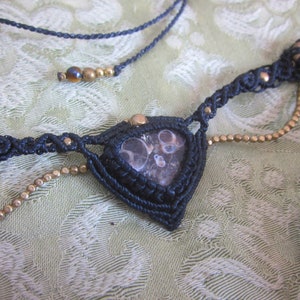 May include: A black macrame necklace with a brown and white agate stone pendant and gold beads.