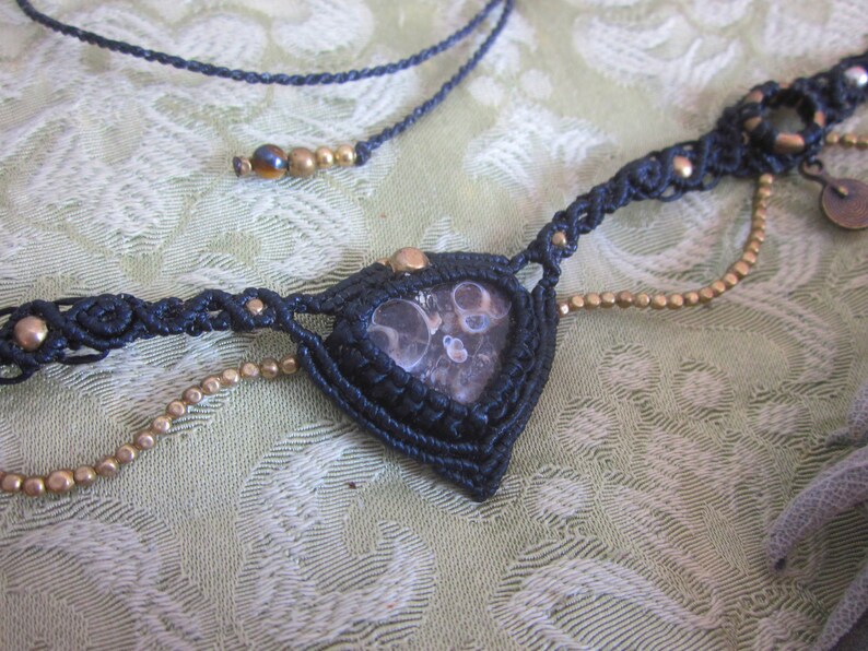 May include: A black macrame necklace with a brown and white agate stone pendant and gold beads.