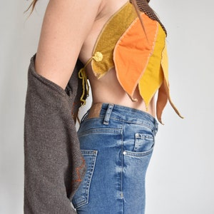 Peut inclure: Un pull marron avec un haut en tissu jaune, orange et marron avec une fermeture &agrave; bouton. Le haut est port&eacute; sur un jean bleu.