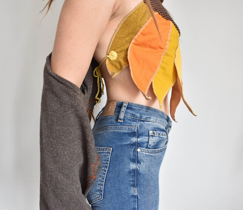 Peut inclure: Un pull marron avec un haut en tissu jaune, orange et marron avec une fermeture &agrave; bouton. Le haut est port&eacute; sur un jean bleu.