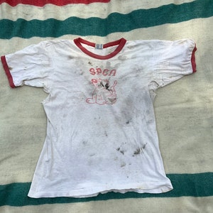 May include: White t-shirt with red trim and a faded graphic of a cat with the word "SPCA" above it.