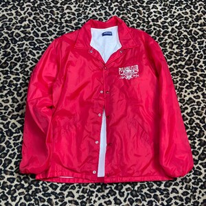May include: Red nylon jacket with a snap closure and a white embroidered logo that says "PULASKI CLUB" on the front.