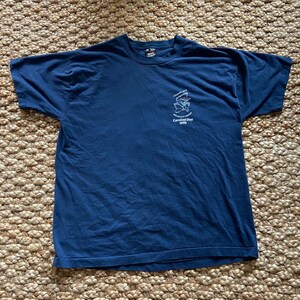May include: A navy blue t-shirt with a white embroidered design featuring a cartoon character and the text "Old Town "Celebration" Walla Walla County Carnival Day 1993".