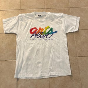 May include: White t-shirt with a colorful "Arts Alive" graphic. The text is in a rainbow gradient with the words "1990 OLEAN NEW YORK" below the main text. The shirt is laid flat.