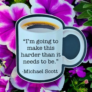 May include: A white coffee mug with a black rim and handle. The mug has a black and white graphic of a coffee cup with the quote "I'm going to make this harder than it needs to be." - Michael Scott.