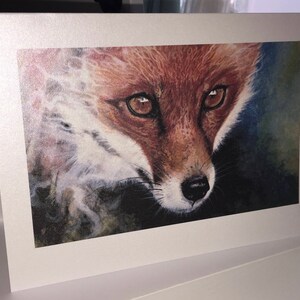 May include: A greeting card featuring a detailed watercolor painting of a fox. The fox has reddish-brown fur, a white chest, and dark eyes. The card is set against a white background.