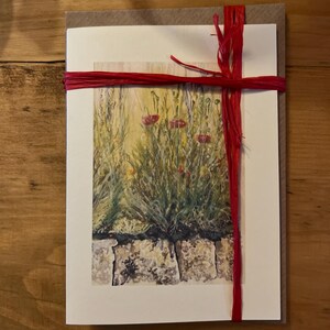 May include: A greeting card with a watercolor painting of red flowers in a field. The card is tied with a red ribbon.