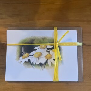 May include: A white card with a drawing of a bouquet of white daisies with yellow centers. The card is tied with a yellow ribbon and is wrapped in a brown envelope.