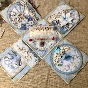 Peut inclure: Une boîte artisanale sur le thème de Noël, aux tons bleu clair et blanc. La boîte présente des éléments décoratifs tels que des découpes en bois, des compositions florales et l'inscription "Merry Christmas". La boîte est décorée avec diverses textures et motifs.