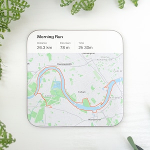 May include: A white square coaster with a map of London showing a running route along the River Thames. The text "Morning Run" is at the top of the coaster, along with the distance, elevation gain, and time of the run: 26.3 km, 78 m, and 2h 30m.
