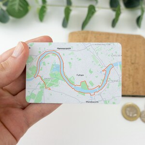 Op de afbeelding: Een witte kaart met een kaart van de Theems in Londen, Engeland. De kaart toont de rivier die door de stad slingert, met de namen van verschillende wijken, waaronder Hammersmith, Fulham en Wandsworth.