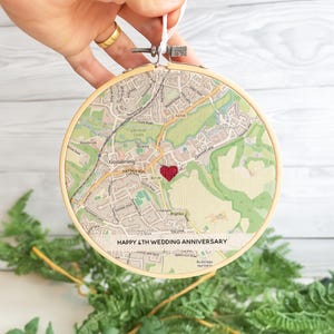 May include: An embroidered map of Godalming, England, in a wooden hoop, featuring a red heart and the text "HAPPY 4TH WEDDING ANNIVERSARY". The map shows local roads and landmarks, perfect for a special anniversary gift.
