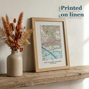 May include: A framed map print with a light wood frame, displayed on a rustic wooden shelf. The map is printed on linen and features a detailed street map with the text "Happy 4th Wedding Anniversary 12th May 2022". A vase with dried flowers is to the left.