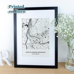 May include: A framed black and white map print with the text "Happy 4th Wedding Anniversary 6th October 2021." The print is set in a white mount and black frame. The words "Printed on linen" are in the upper left corner.