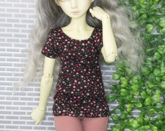 May include: A doll wearing a black and pink floral print short-sleeved shirt and pink leggings. The doll has long, wavy, silver hair and yellow eyes.